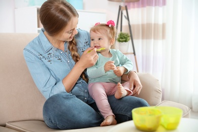 Caring mother feeding her cute little baby with healthy food at home