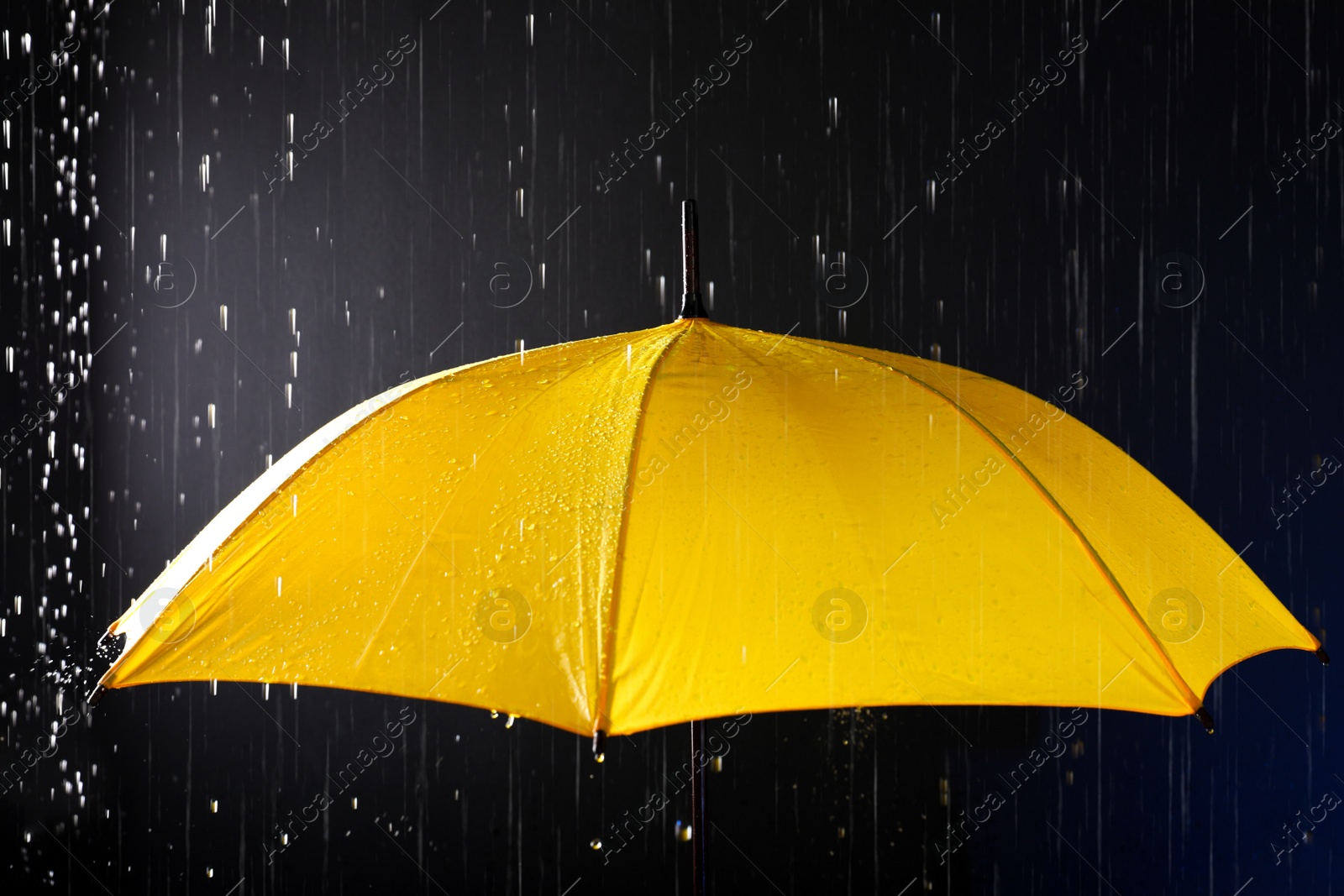 Photo of Bright umbrella under rain on dark background