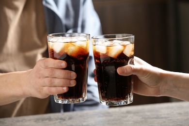 Couple with glasses of cold cola at table indoors, closeup