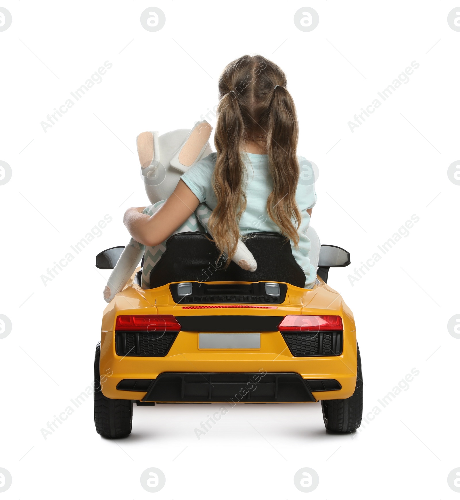 Photo of Cute little girl with toy bunny driving children's car on white background, back view