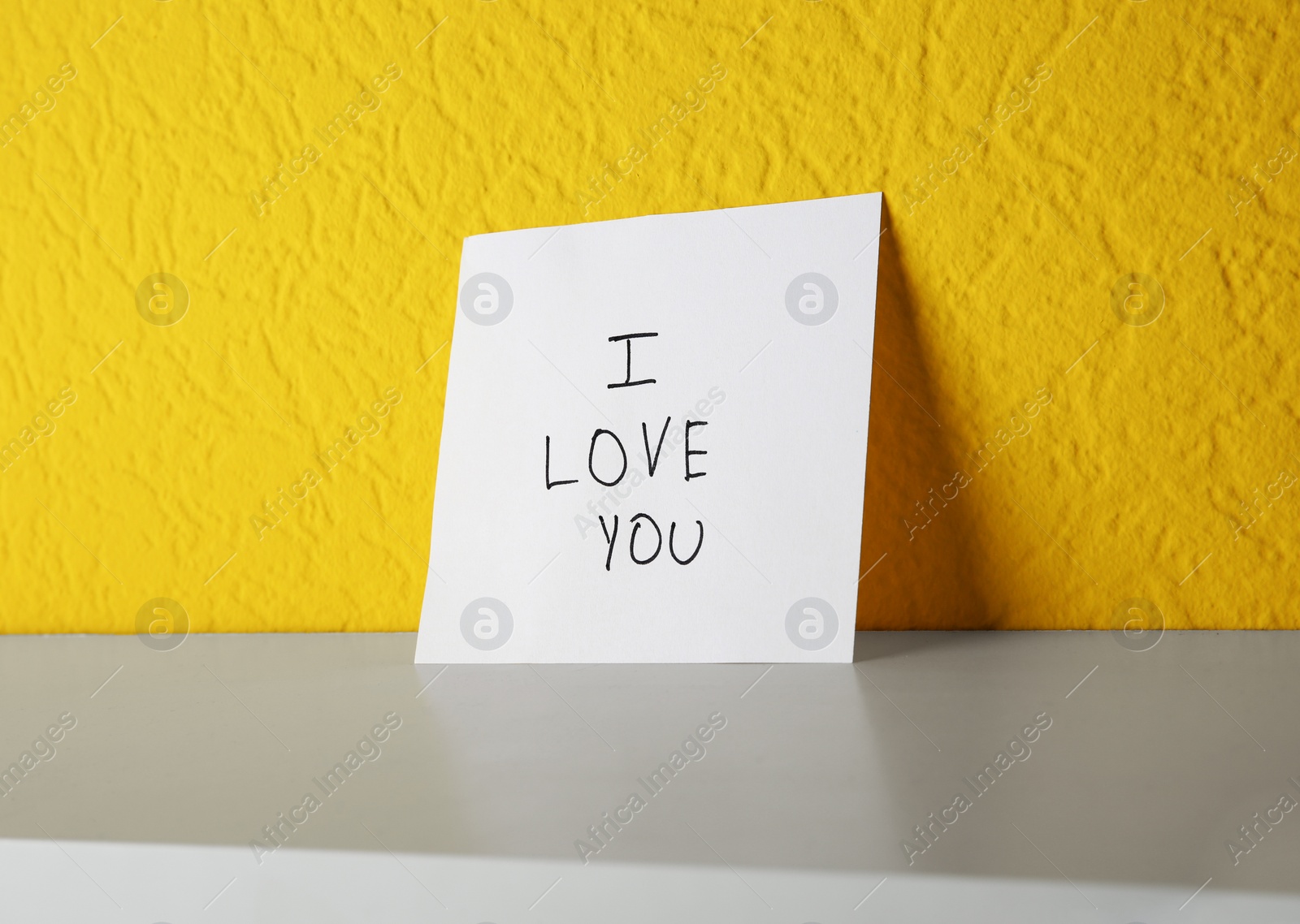 Photo of Paper with text I LOVE YOU on shelf at color wall