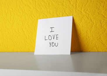 Paper with text I LOVE YOU on shelf at color wall