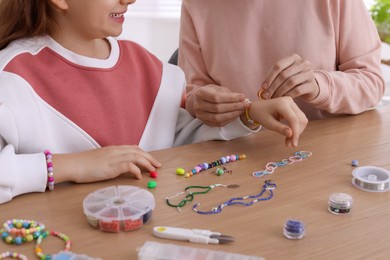 Photo of Mother with her daughter making beaded jewelry at home, closeup