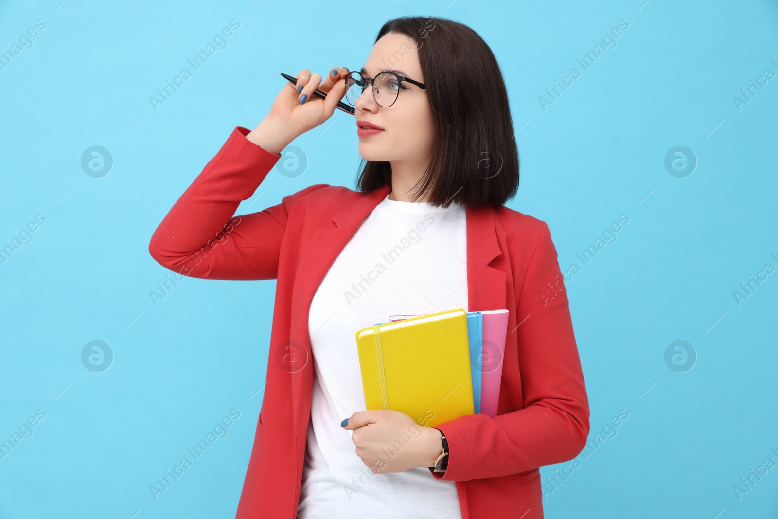 Photo of Young intern with notebooks and pen on light blue background