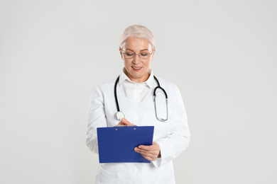 Photo of Mature doctor with clipboard on light grey background