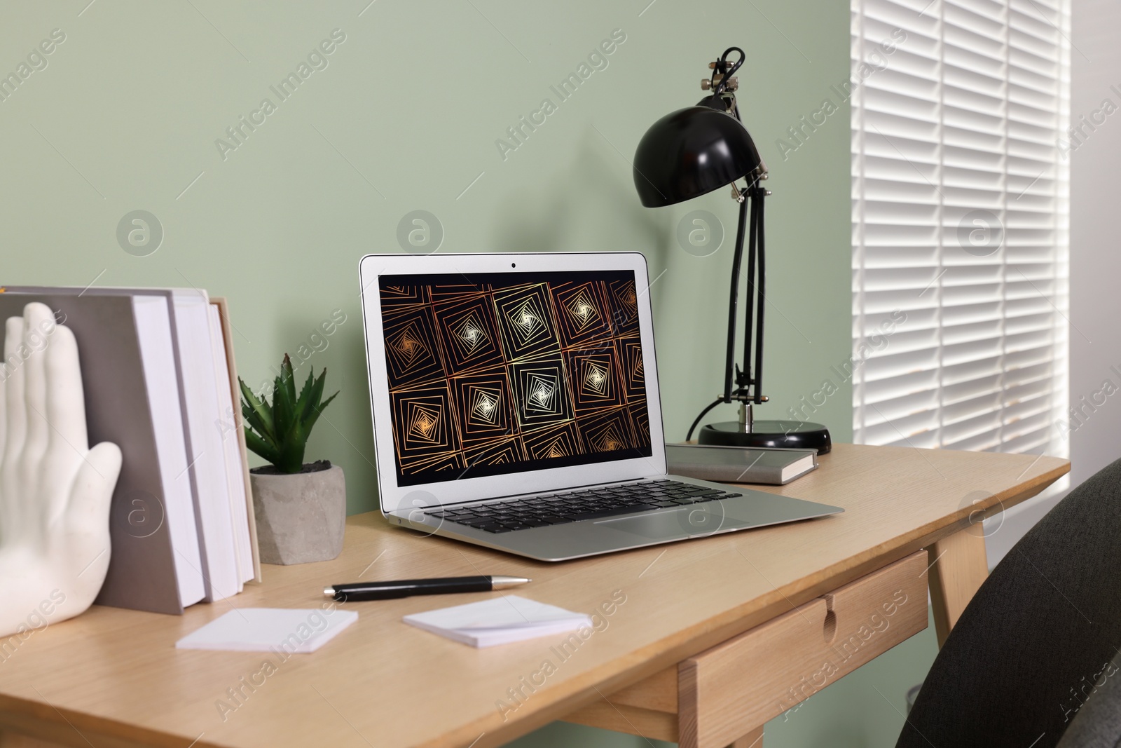 Photo of Modern laptop, books, lamp and stationery on wooden desk near green wall. Home office