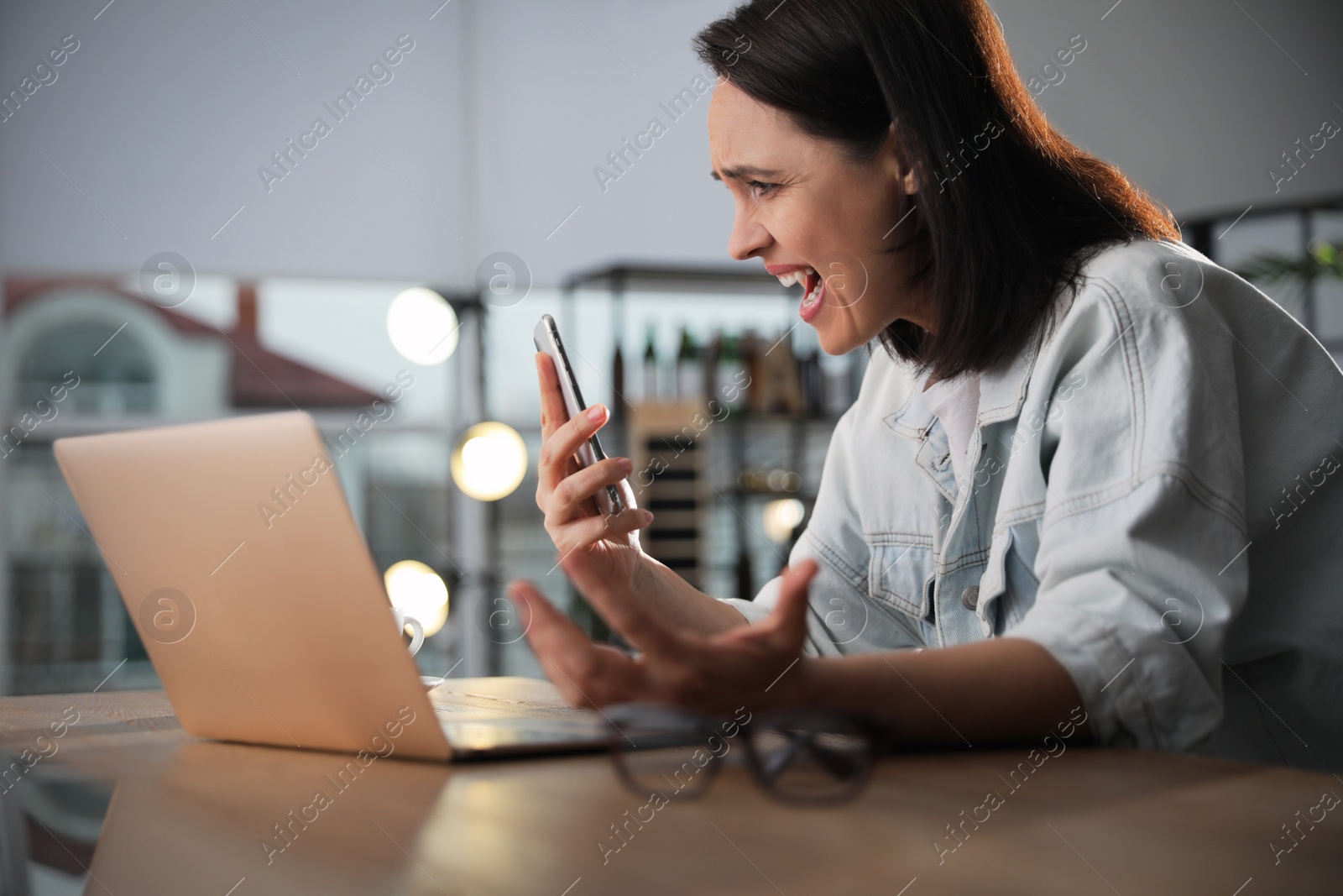 Photo of Emotional woman with smartphone at table in office. Online hate concept