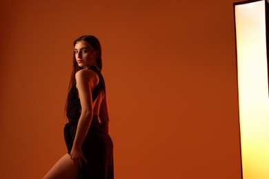 Photo of Beautiful woman in black dress posing on brown background. Space for text