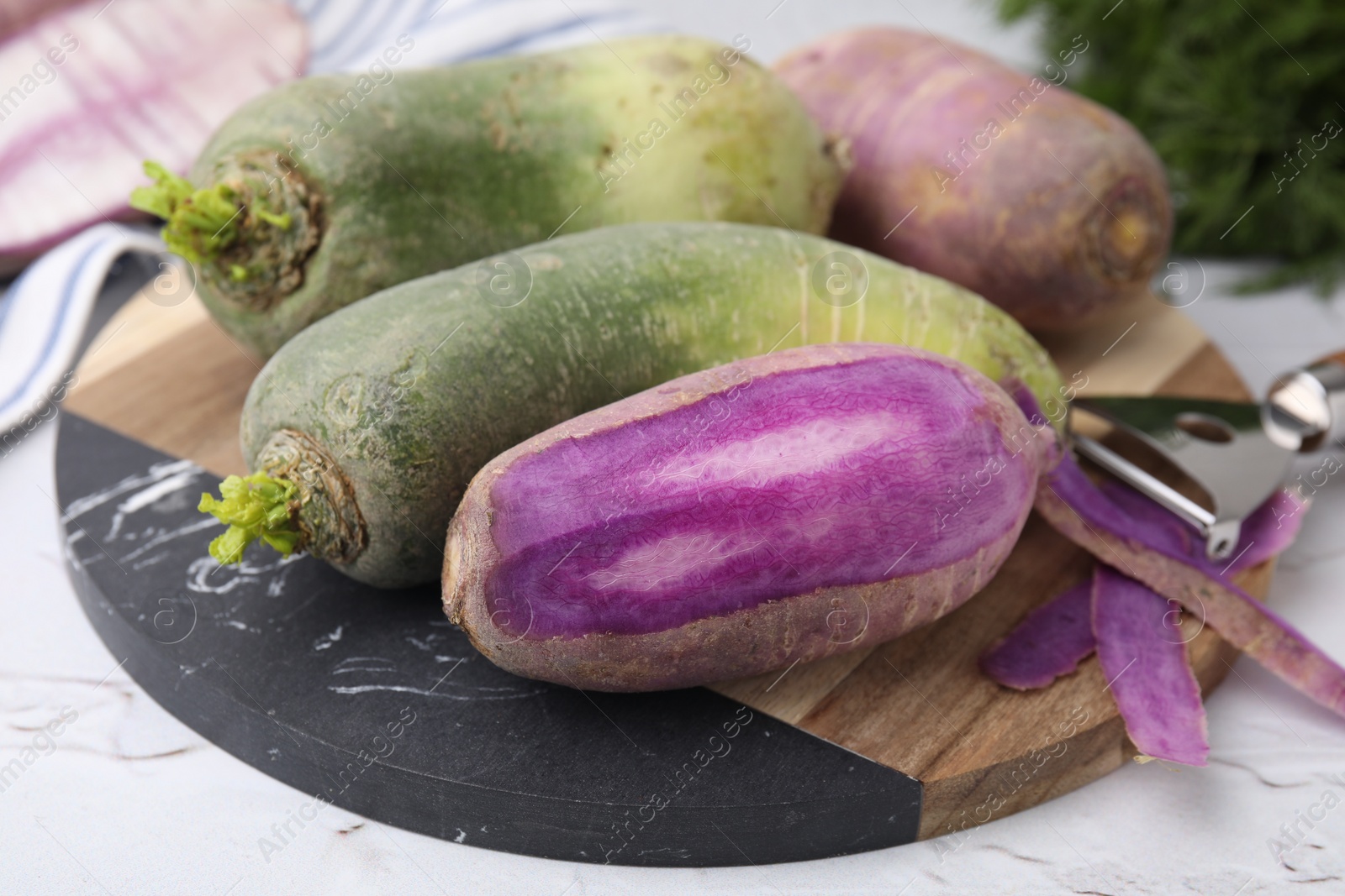 Photo of Purple and green daikon radishes on white textured table, closeup