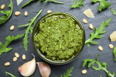 Bowl of tasty arugula pesto and ingredients on black table, flat lay