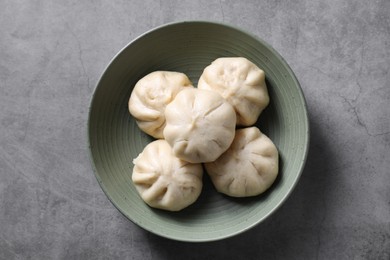 Delicious bao buns (baozi) in bowl on grey textured table, top view