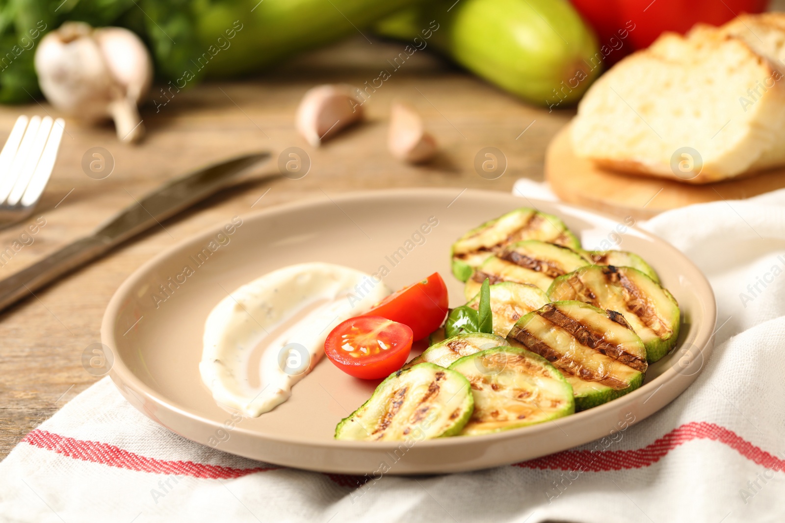 Photo of Delicious grilled zucchini slices served with sauce and tomatoes on wooden table, closeup