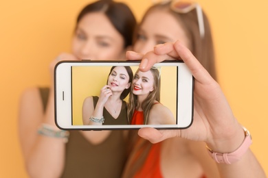 Attractive young women taking selfie on color background, closeup