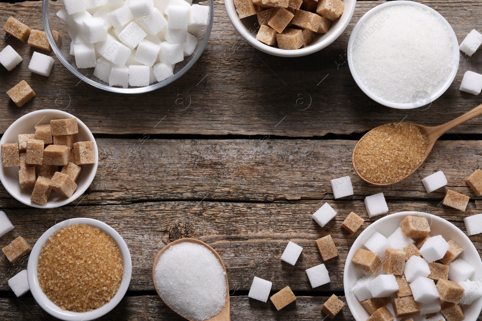 Photo of Frame of bowls and spoons with different types of sugar on wooden table, flat lay. Space for text