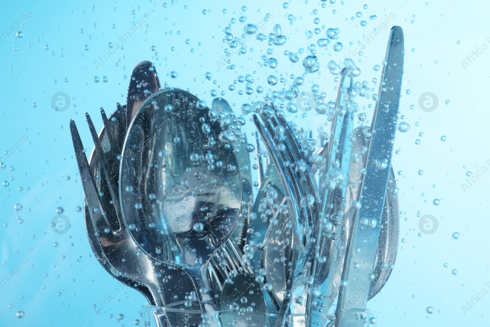 Photo of Washing silver cutlery in water on light blue background, closeup