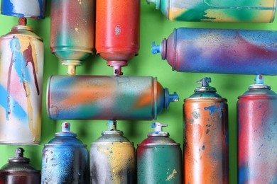 Many spray paint cans on green background, flat lay