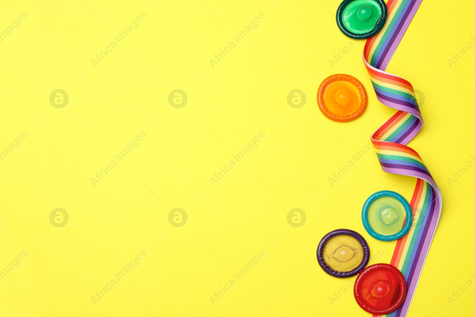 Photo of Flat lay composition with colorful condoms and rainbow ribbon on yellow background, space for text. LGBT concept