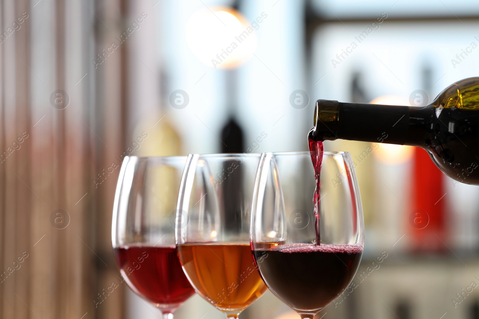 Photo of Pouring red wine from bottle into glass indoors, closeup