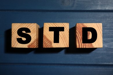 Photo of Wooden cubes with letters STD (sexually transmitted diseases) on blue table, flat lay