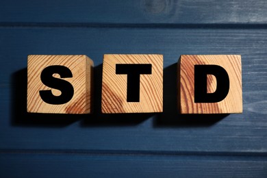 Wooden cubes with letters STD (sexually transmitted diseases) on blue table, flat lay