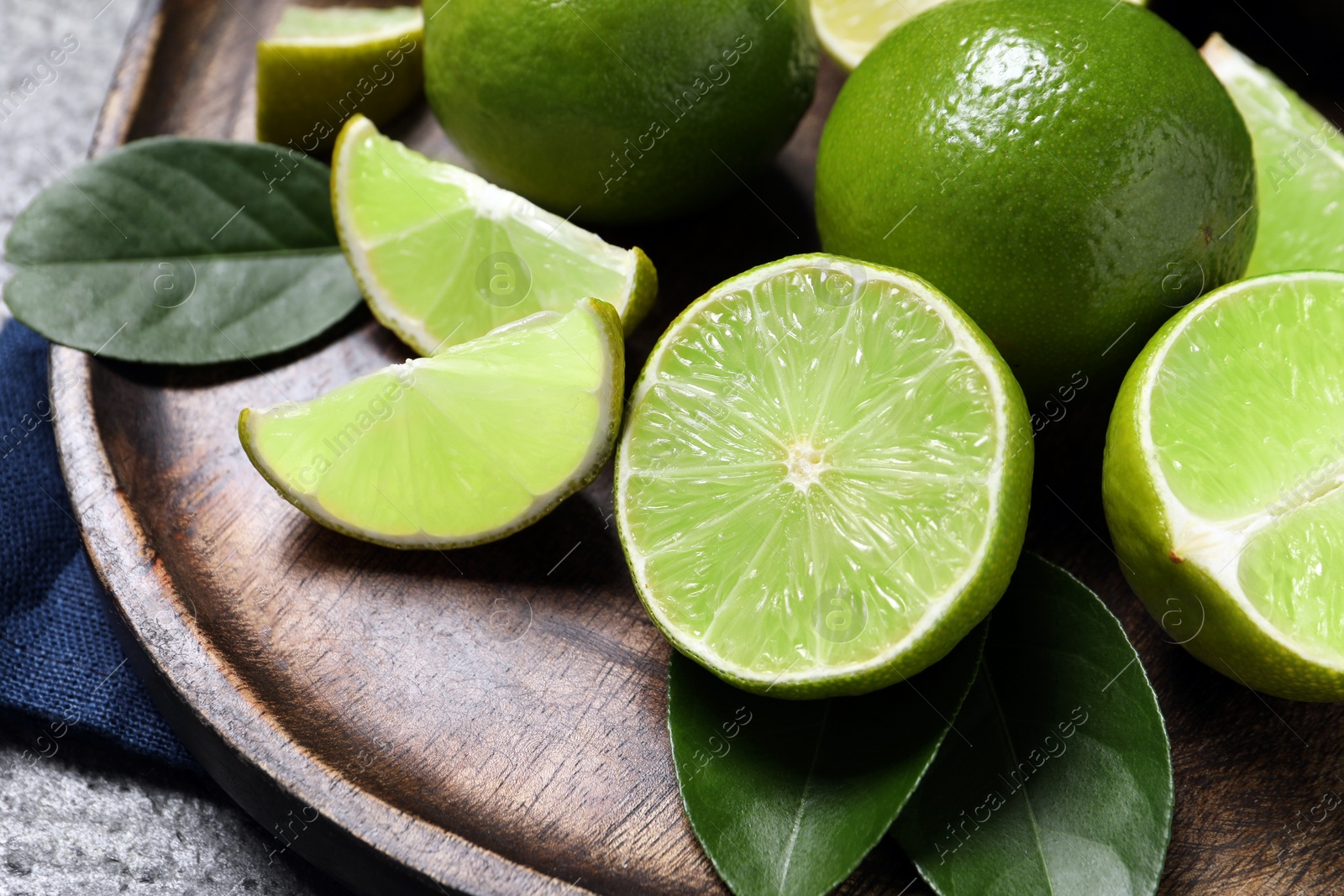 Photo of Fresh ripe limes and leaves on grey table, closeup