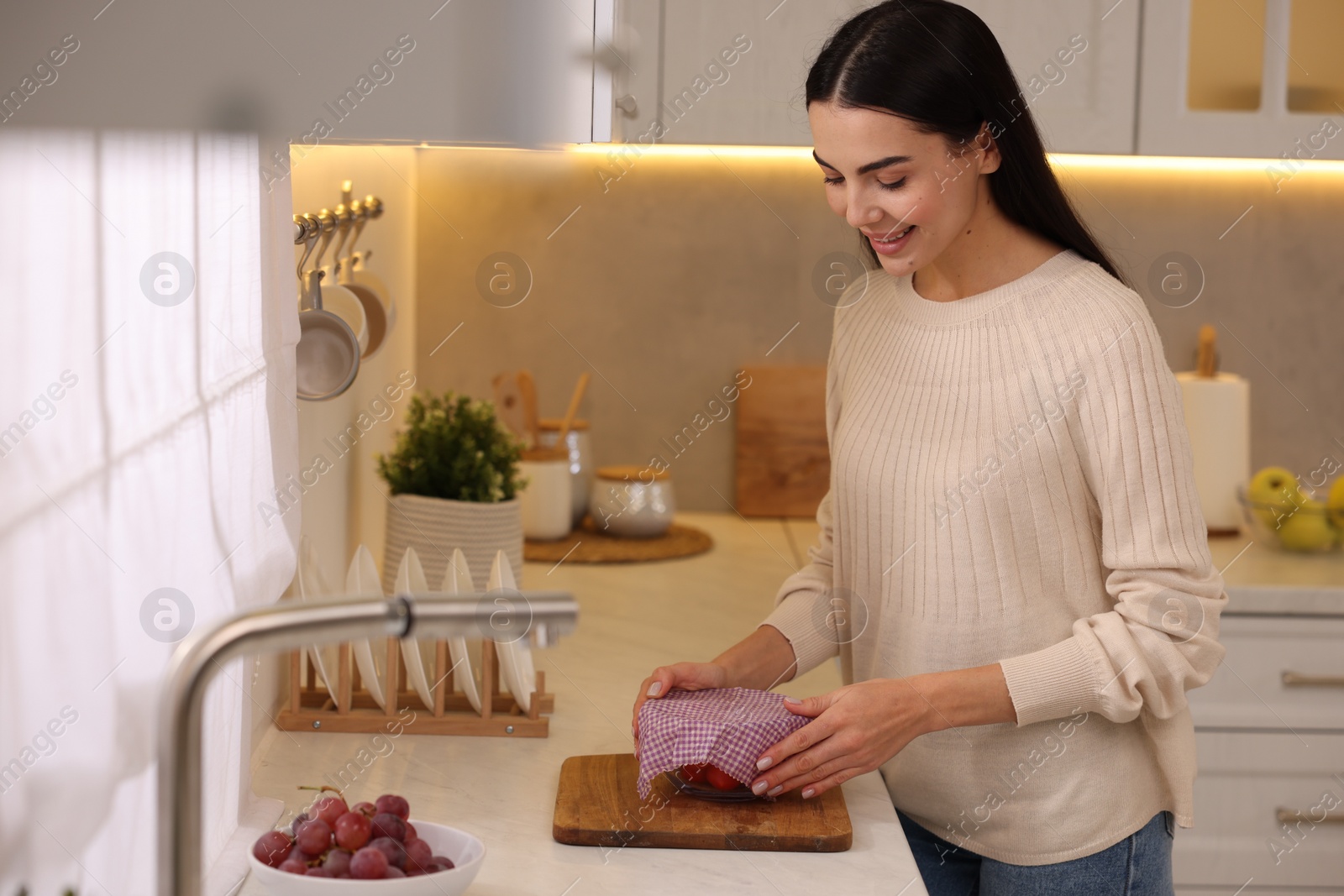 Photo of Happy woman packing bowl into beeswax food wrap at countertop in kitchen