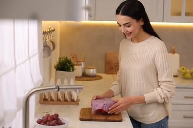 Happy woman packing bowl into beeswax food wrap at countertop in kitchen