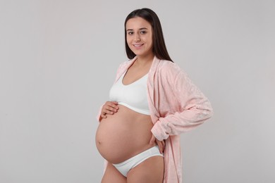 Beautiful pregnant woman in stylish comfortable underwear and robe on grey background