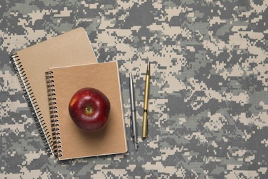 Photo of Notebooks, pens and apple on camouflage background, flat lay with space for text. Military education