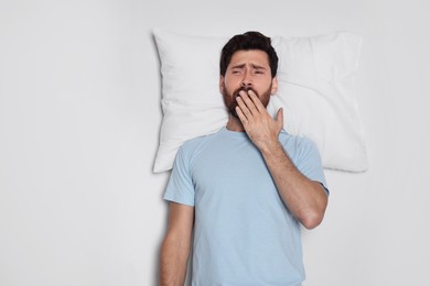 Photo of Handsome man with soft pillow yawns on light grey background