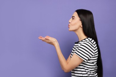 Beautiful young woman blowing kiss on purple background. Space for text