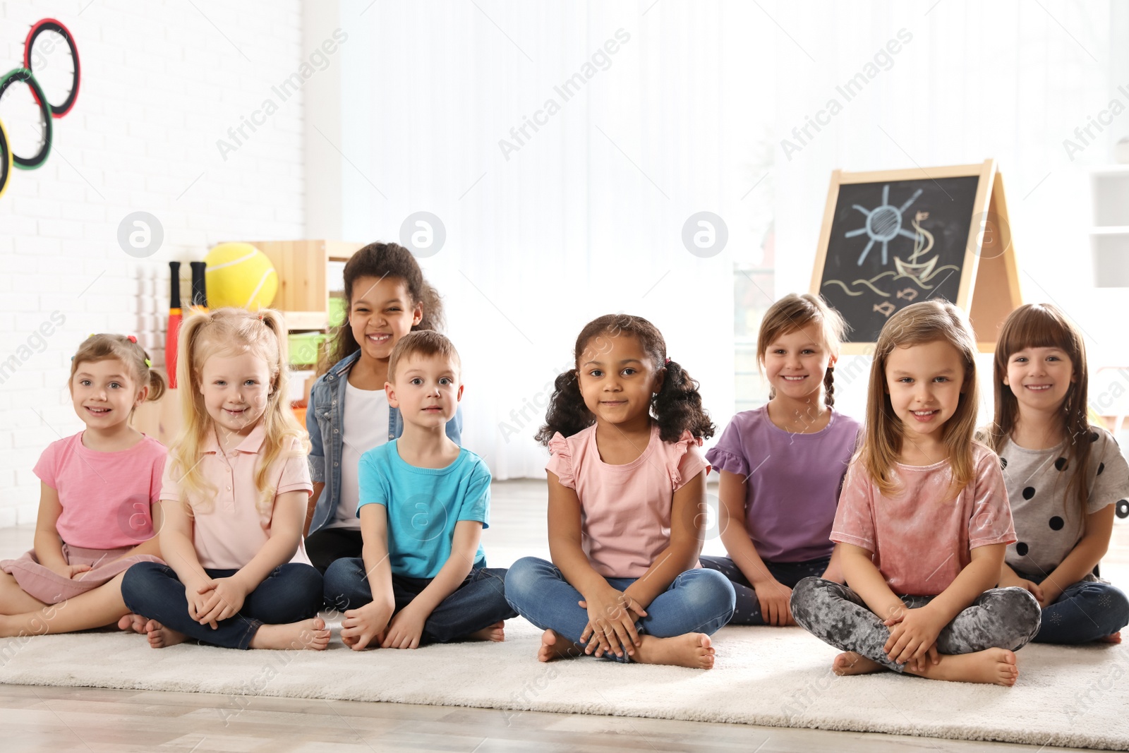 Photo of Group of cute little children sitting on floor indoors. Kindergarten playtime activities