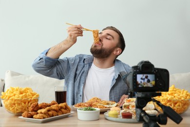 Photo of Food blogger recording eating show on camera against light background. Mukbang vlog