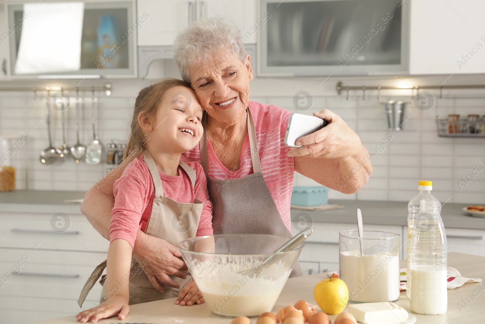 Photo of Little girl and her grandmother taking selfie in kitchen