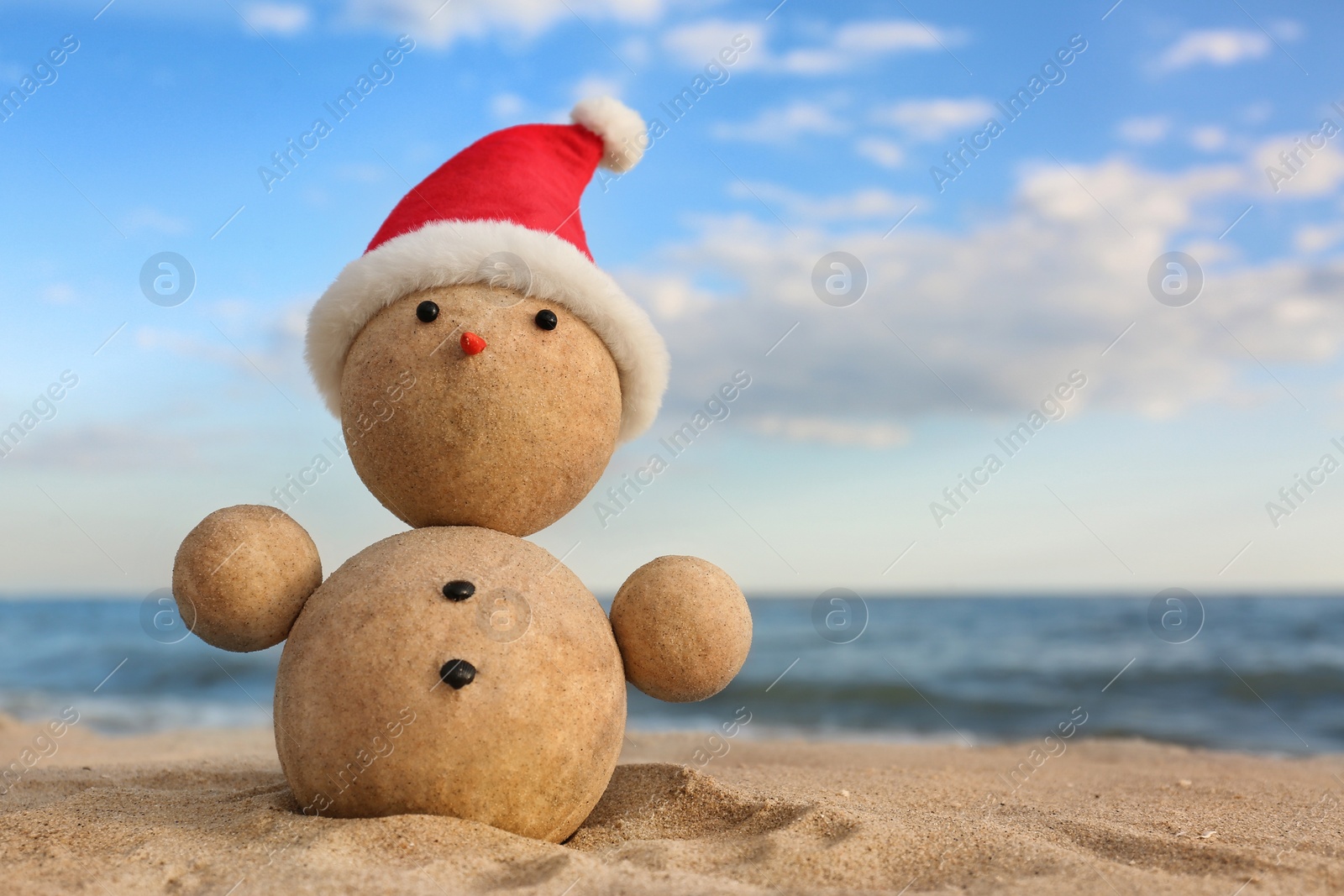 Photo of Snowman made of sand with Santa hat on beach near sea, space for text. Christmas vacation