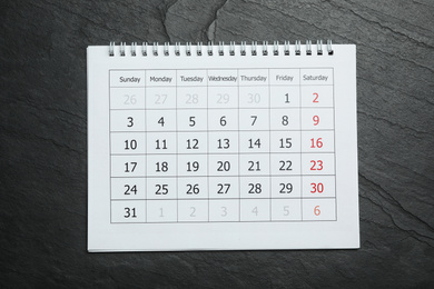 Paper calendar on black stone background, top view