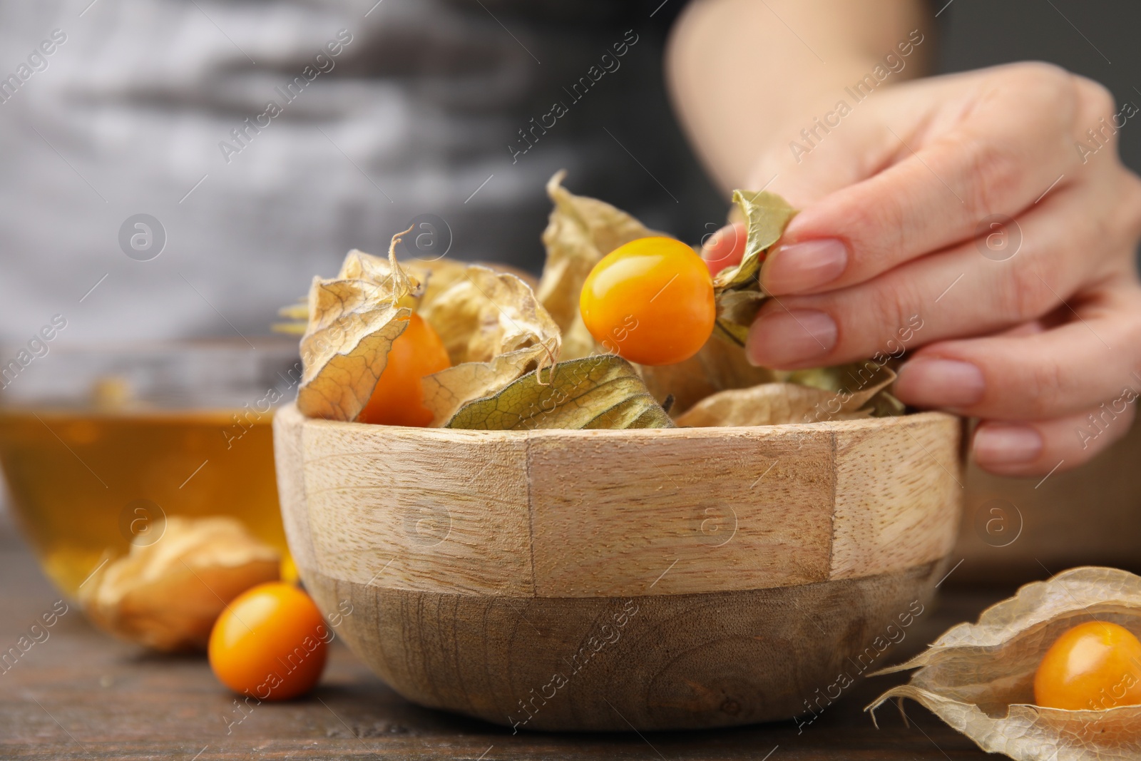 Photo of Woman peeling physalis fruit from calyxes at wooden table, closeup