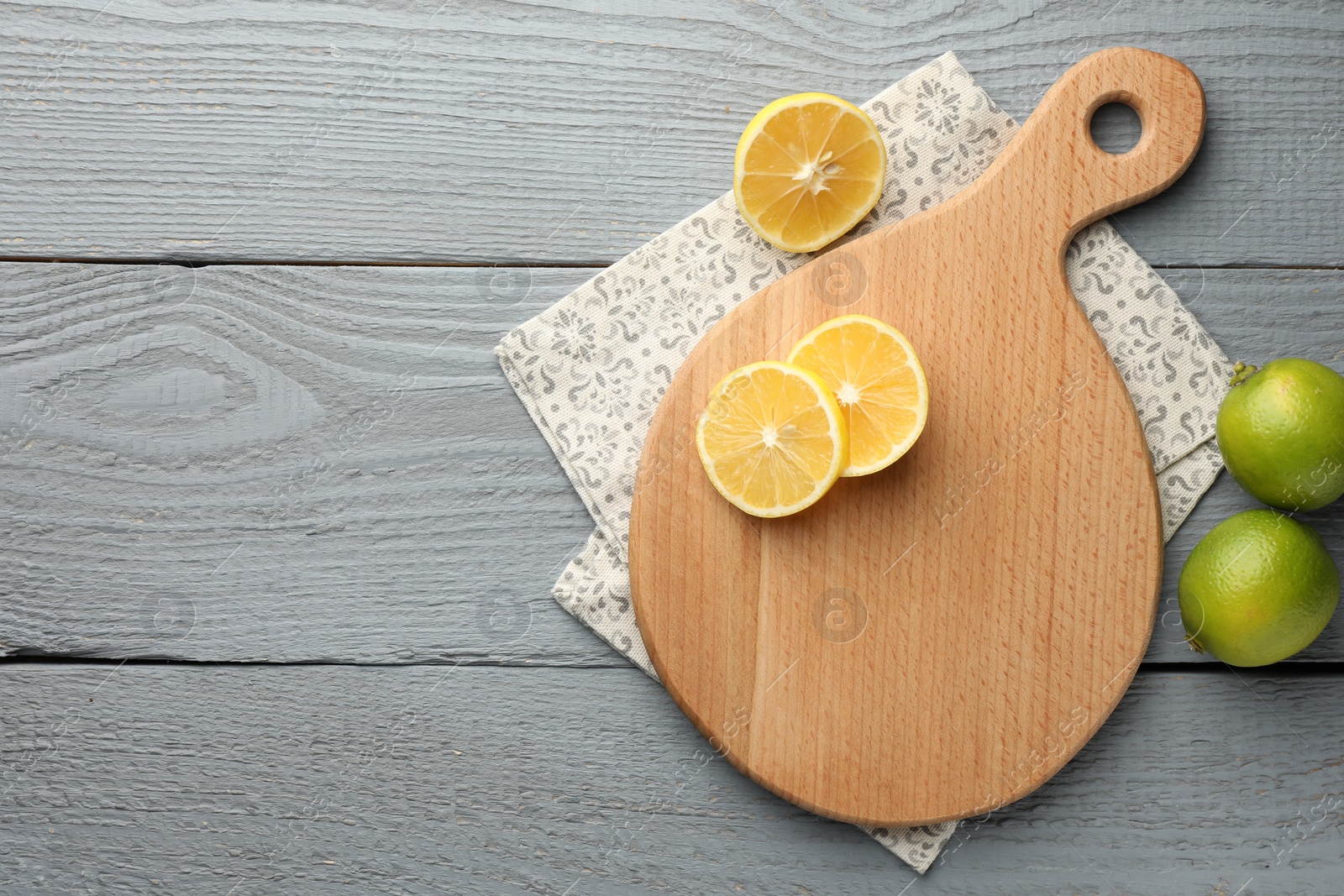 Photo of Cutting board, lemon and limes on grey wooden table, flat lay. Space for text