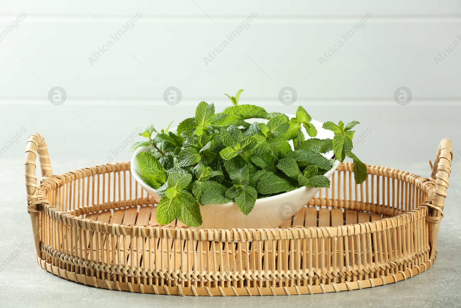 Photo of Wicker tray with bowl of fresh green mint leaves on grey table