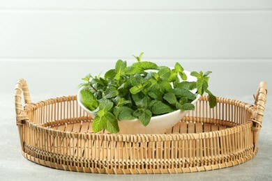 Wicker tray with bowl of fresh green mint leaves on grey table