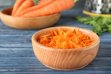 Photo of Bowl of grated carrot on wooden table, closeup