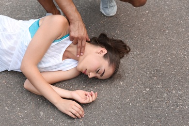 Photo of Young man checking pulse of unconscious woman on street