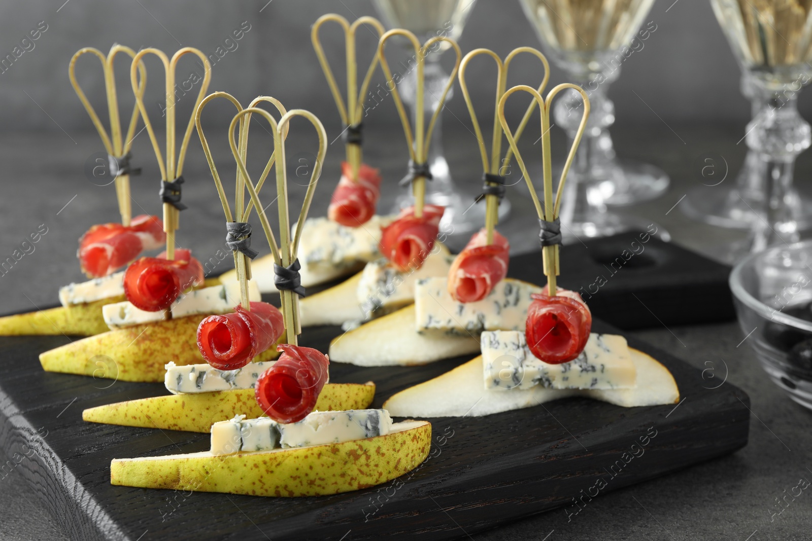 Photo of Tasty canapes with pears, blue cheese and prosciutto on grey table, closeup