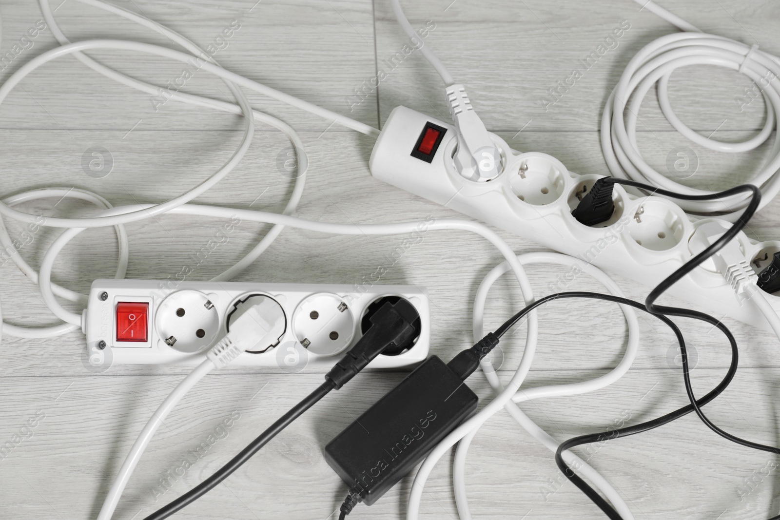Photo of Power strips with different electrical plugs on white floor, flat lay