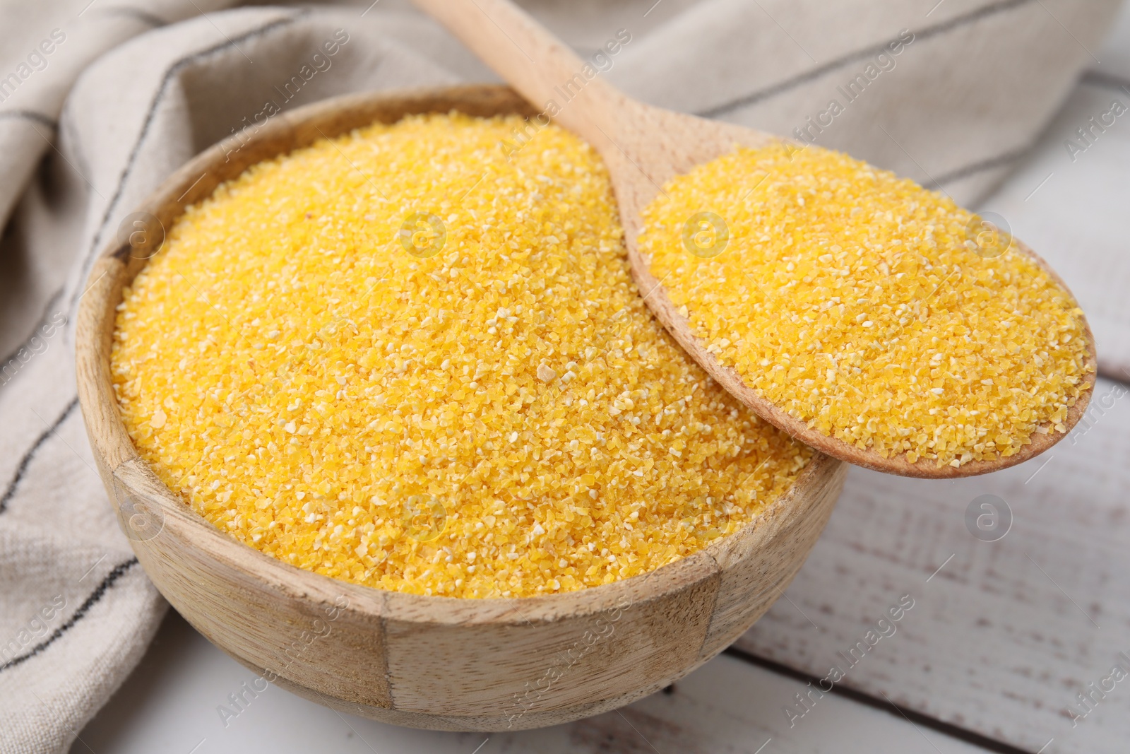 Photo of Raw cornmeal in bowl and spoon on light wooden table, closeup