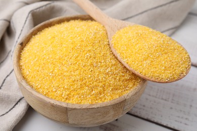 Photo of Raw cornmeal in bowl and spoon on light wooden table, closeup