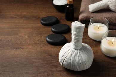 Photo of Herbal massage bag, spa stones and candles on wooden table. Space for text