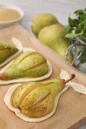 Photo of Board with raw dough, fresh pears and mint on table, closeup