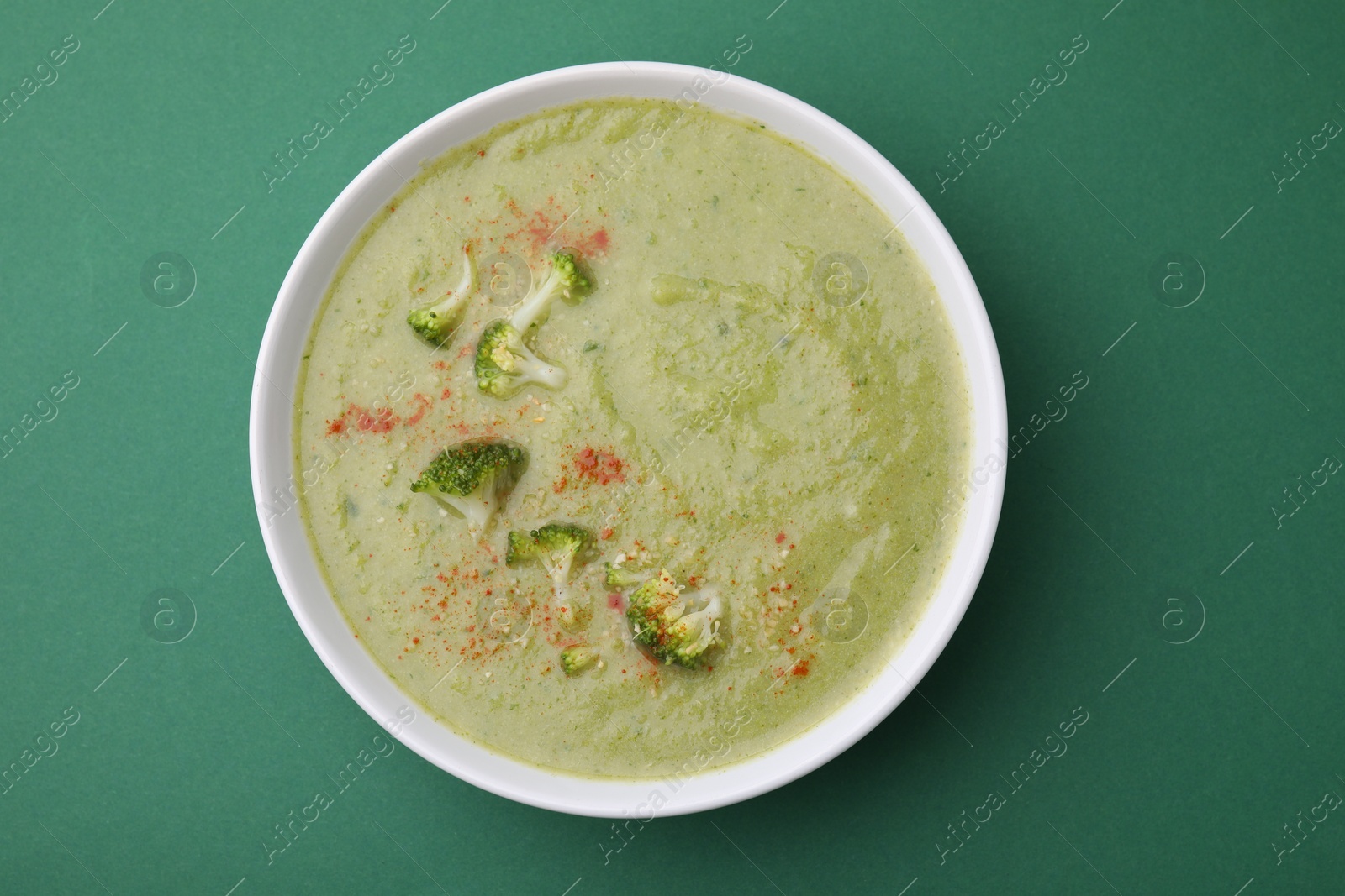 Photo of Delicious broccoli cream soup on green background, top view