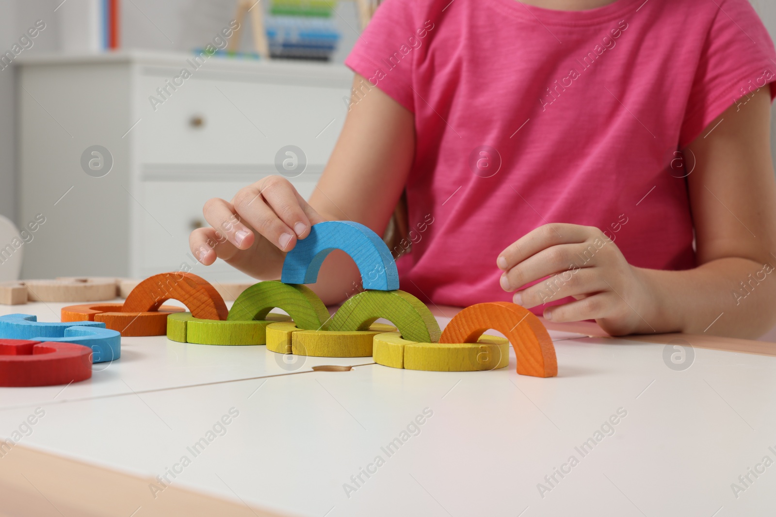 Photo of Motor skills development. Girl playing with colorful wooden arcs at white table indoors, closeup